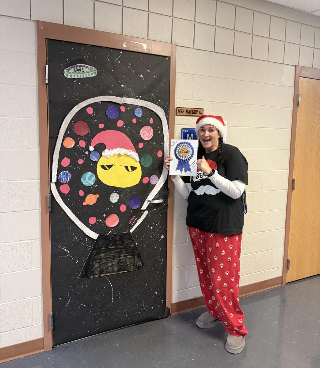 Mrs. Mackey stands beside her decked out door, proudly holding her first place certificate.