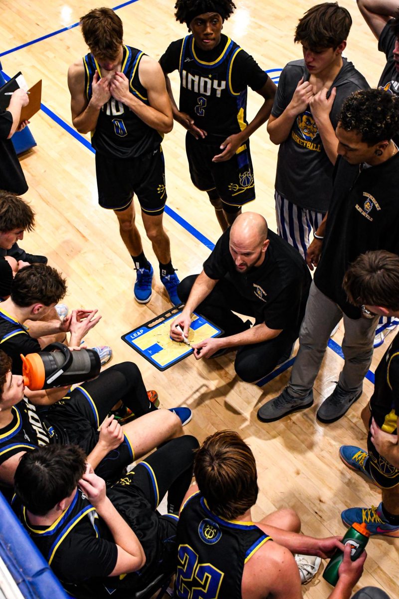 The IHS Boys Varsity Basketball team in a huddle during a timeout listening to Coach Grendel.